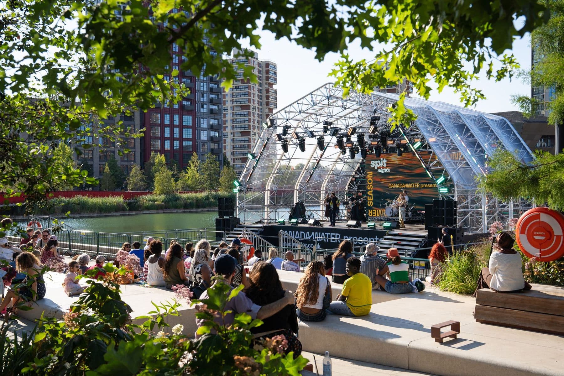 Vasaros festivalio publika prie vandens, matoma pro medžius